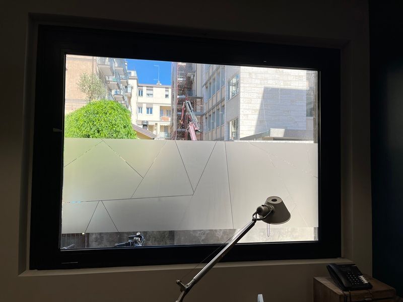 Finestra di un ufficio con vista sugli edifici della città, con una lampada da scrivania in primo piano e vetro inferiore satinato.
