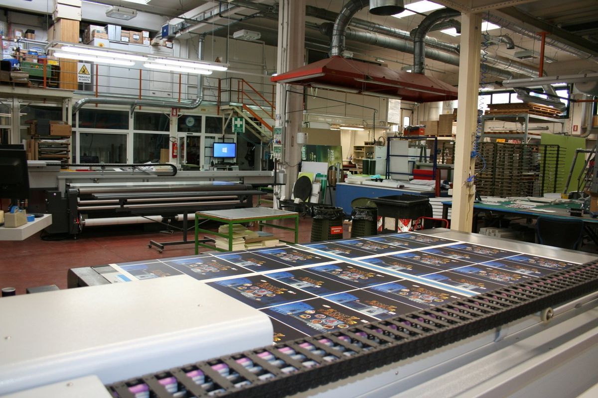Stabilimento industriale con grandi tavoli da taglio, nastri trasportatori e materiali impilati.