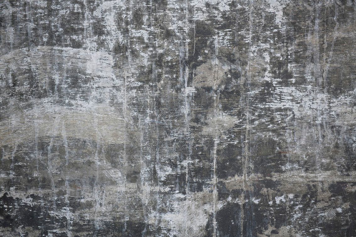 Muro di cemento grigio e deteriorato, con vernice scrostata e macchie verticali.