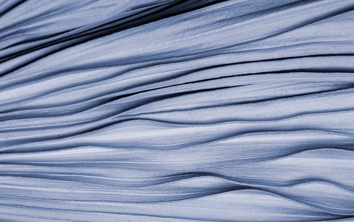 Primo piano di pieghe di tessuto azzurro sovrapposte con morbide increspature diagonali.