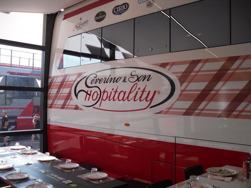 Autobus turistico rosso e bianco con tavoli per banchetti all'interno, recante la scritta