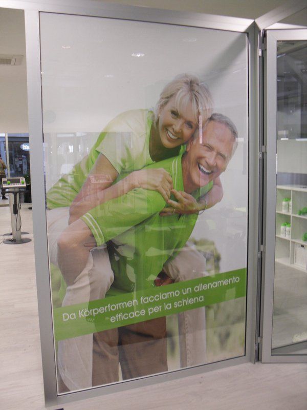 Coppia sorridente in uno showroom, la donna a cavalcioni dell'uomo dietro una porta a vetri con un'insegna verde