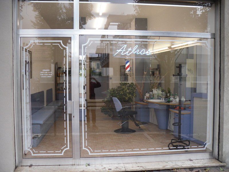 Vetrina di un salone da parrucchiere con ante in vetro, finiture bianche e palo da barbiere all'interno.