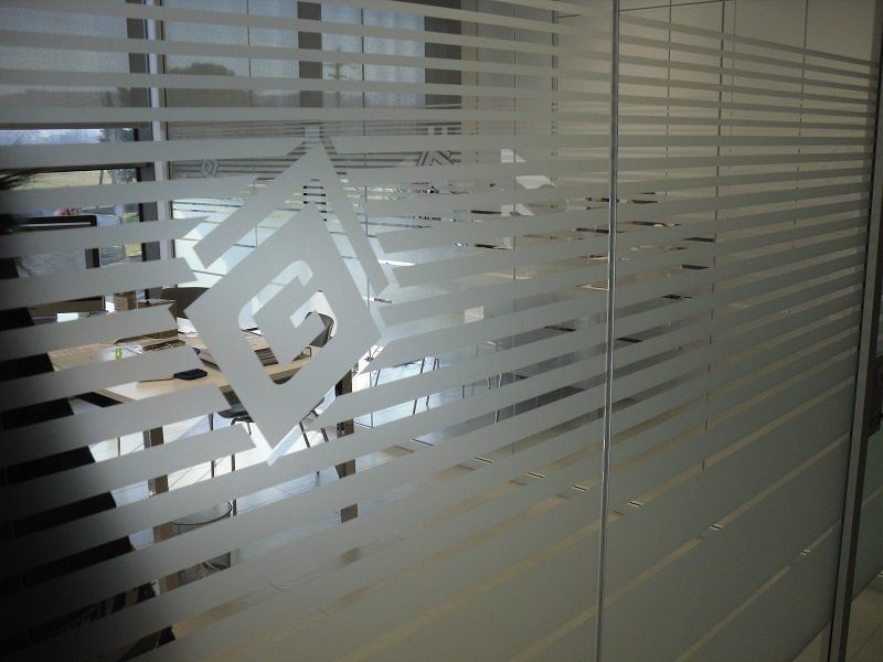 Parete divisoria per ufficio in vetro satinato con strisce orizzontali e decalcomania con logo geometrico.