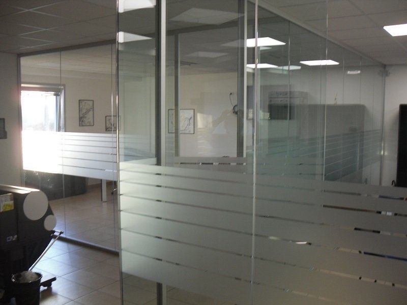 Interno di un ufficio con pareti in vetro, strisce satinate e luci a soffitto che si riflettono sulle pareti.