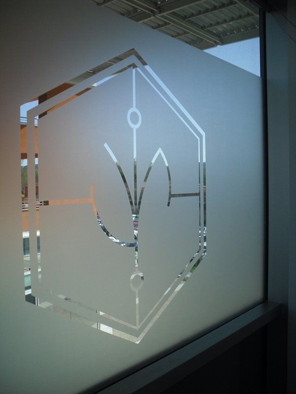 Pannello in vetro satinato con logo geometrico bianco e motivo a foglie in un ambiente d'ufficio interno.