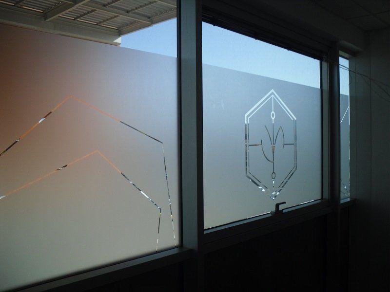 Parete divisoria per ufficio in vetro satinato con logo geometrico inciso, in un corridoio moderno.