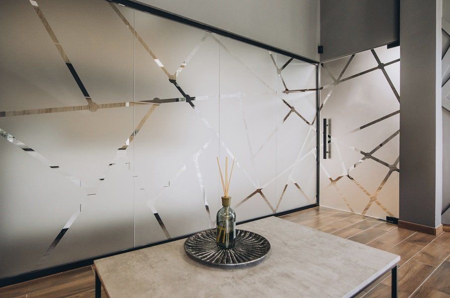 Sala da pranzo moderna con parete in vetro satinato, tavolo in legno e centrotavola decorativo con candele.