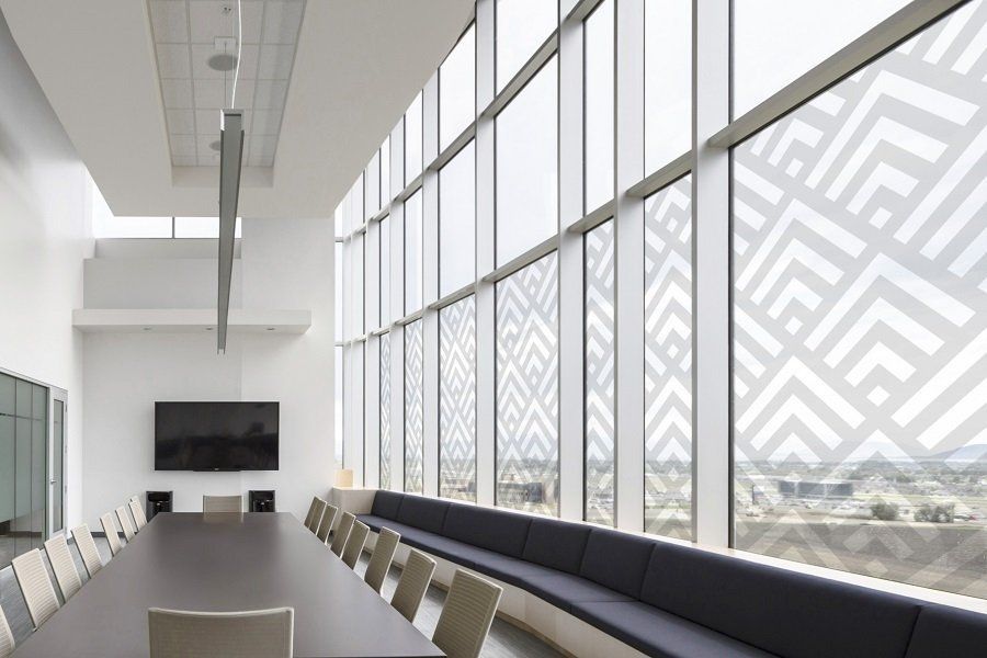 Luminosa sala conferenze moderna con lungo tavolo, sedie e vetrate a tutta altezza che si affacciano su un esterno decorato.