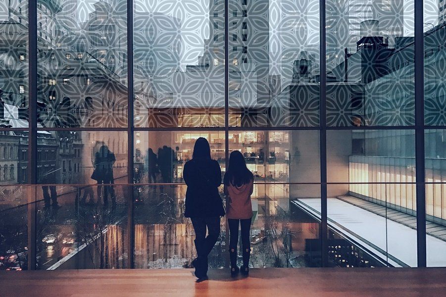Due persone si trovano in una moderna hall di vetro con pareti decorate e riflessi sul pavimento.