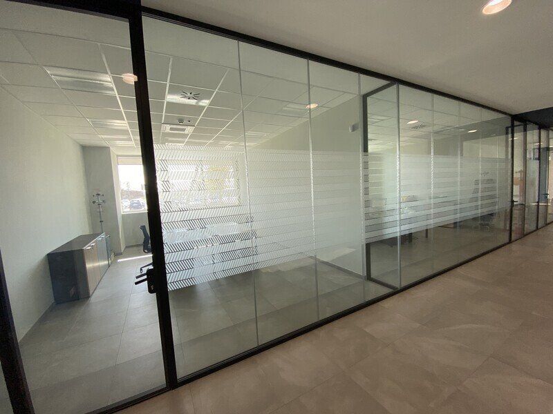 Corridoio ufficio con pareti in vetro, pannelli satinati per sala riunioni e moquette beige.