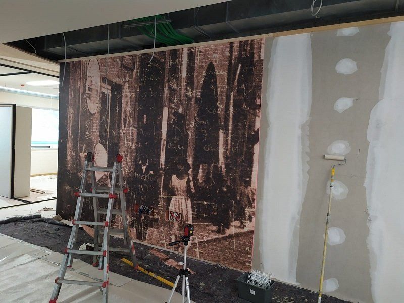Area di lavoro con scala, murale su muro di mattoni e parete in cartongesso parzialmente dipinta.
