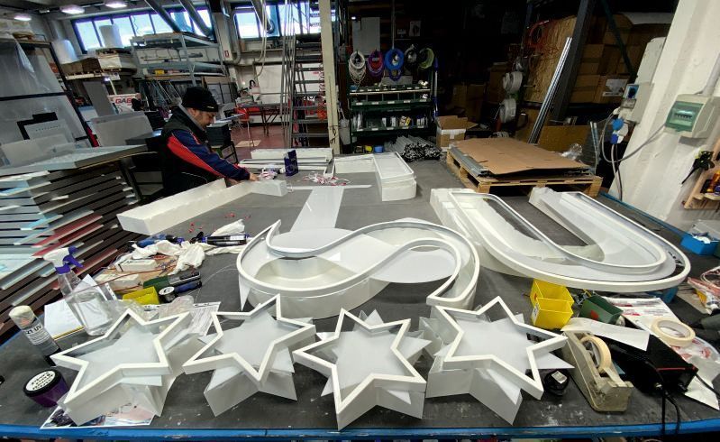 Tavolo da lavoro con grandi sagome bianche a forma di stella e ovale in un'officina, circondato da attrezzi e materiali.