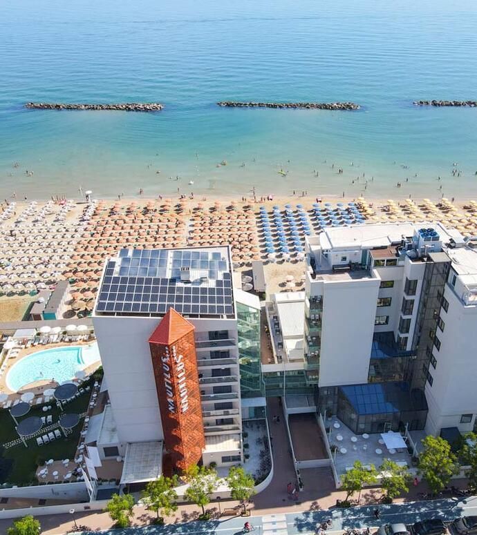 Veduta aerea di una spiaggia con file di ombrelloni, bagnanti e edifici di hotel sul lungomare.