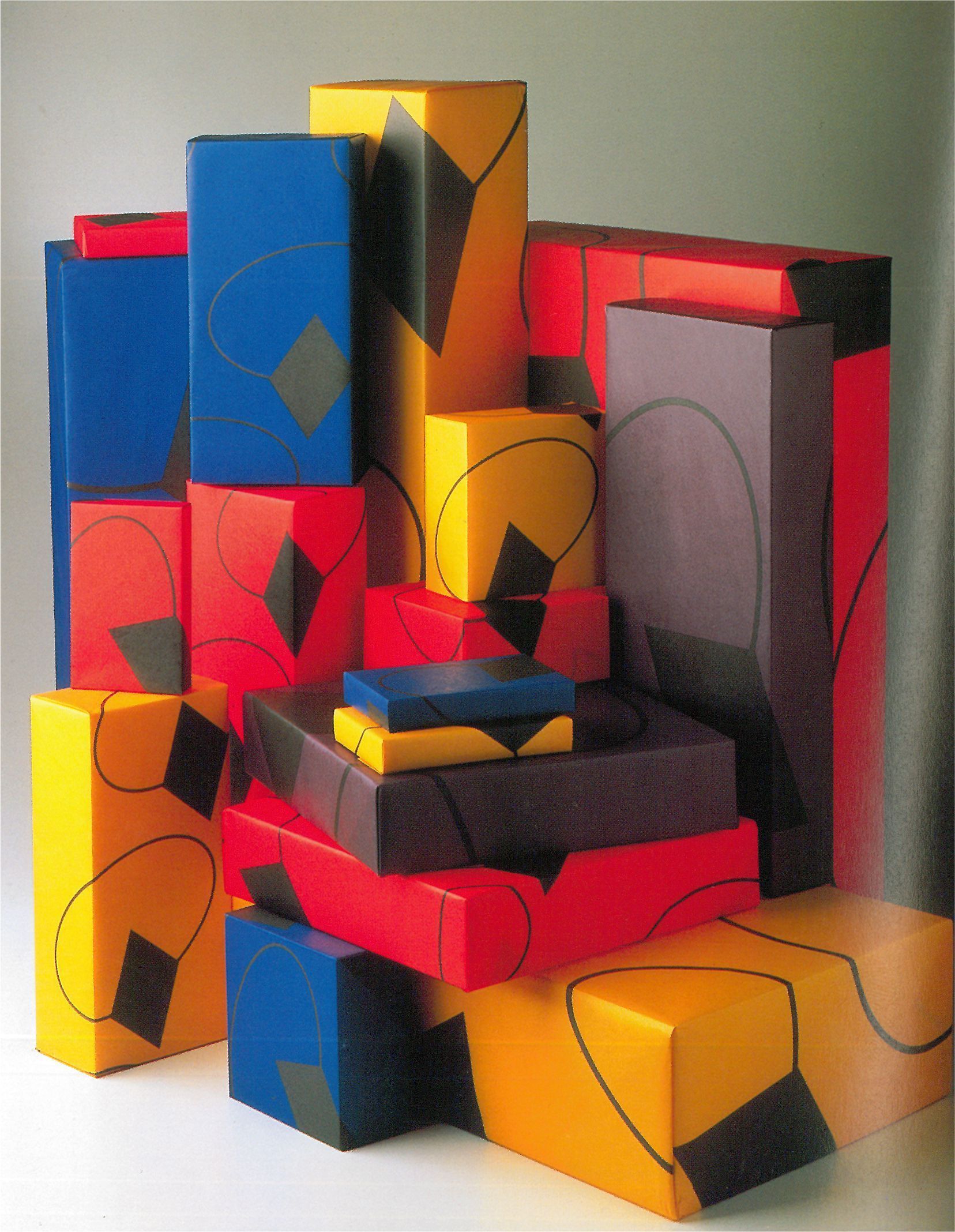 In una natura morta, sono impilati blocchi geometrici astratti e colorati, con forme rosse, blu, gialle e nere.