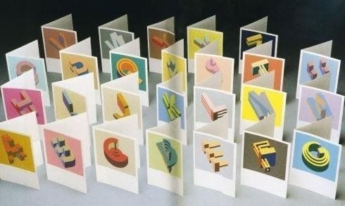 Cartoncini di carta colorata piegati, disposti in fila, ognuno con una piccola illustrazione geometrica.