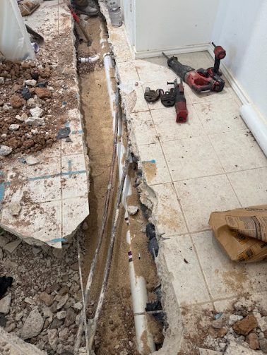 A person wearing white protective gear installs metal piping in a cramped space lined with reflective insulation.