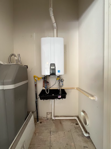 Tankless water heater installation on a wall featuring copper piping, filters, an expansion tank, and electrical controls.