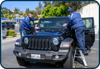 Two men are working on a jeep in a parking lot.