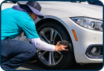 A man in a blue shirt is cleaning the wheel of a white car.