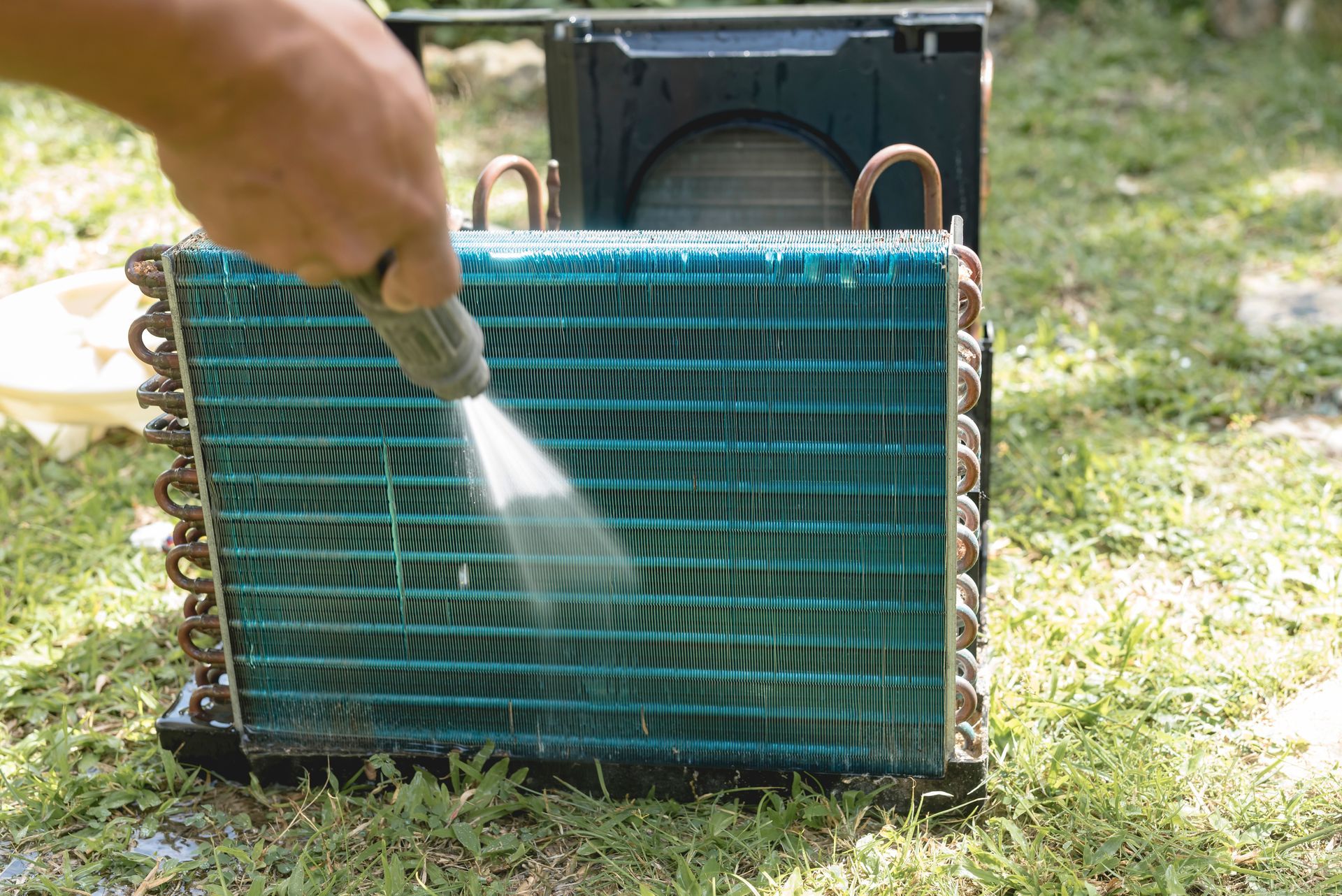 Hand spraying water on a green radiator or AC condenser outdoors
