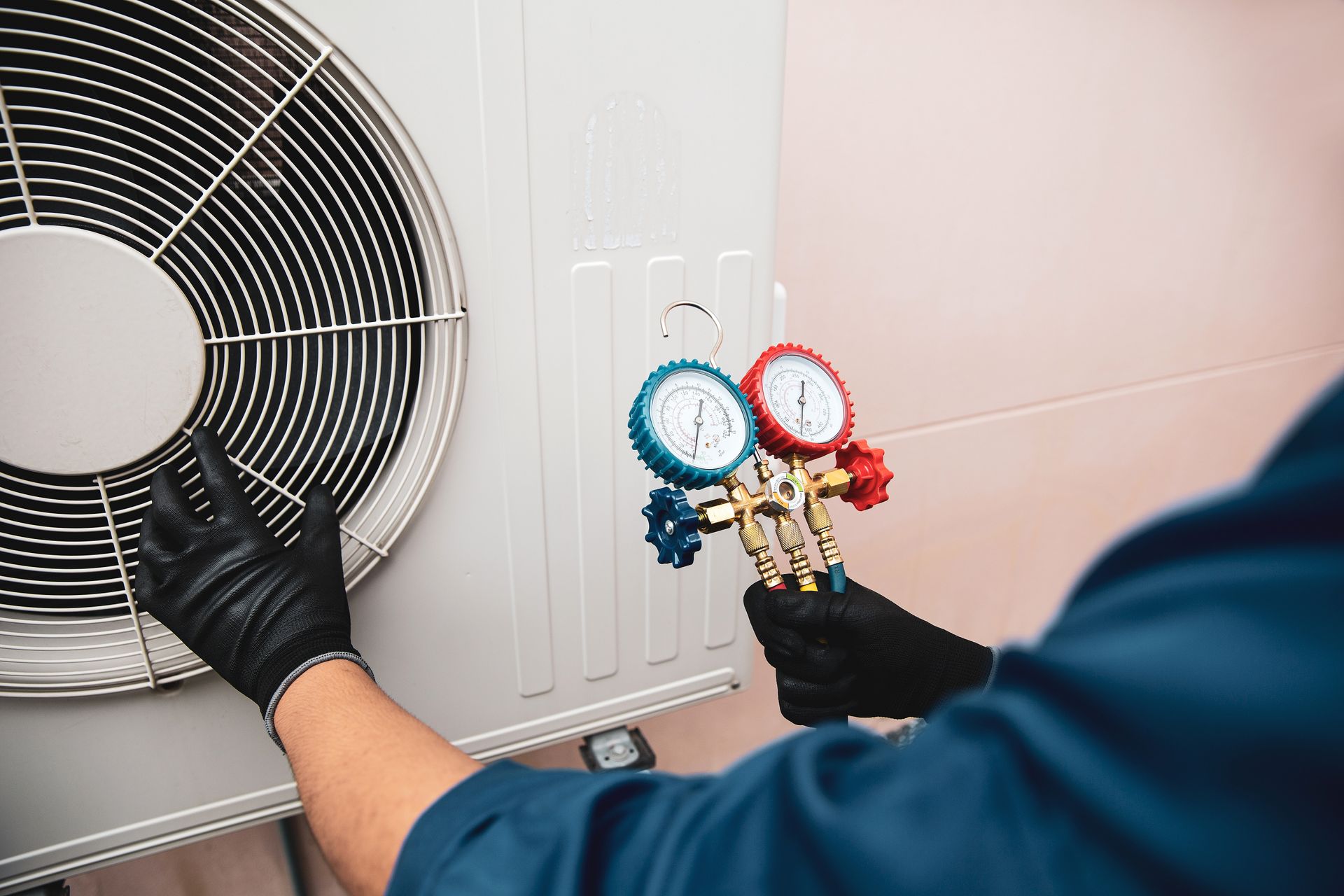 Technician testing an HVAC unit with manifold gauges beside a large fan