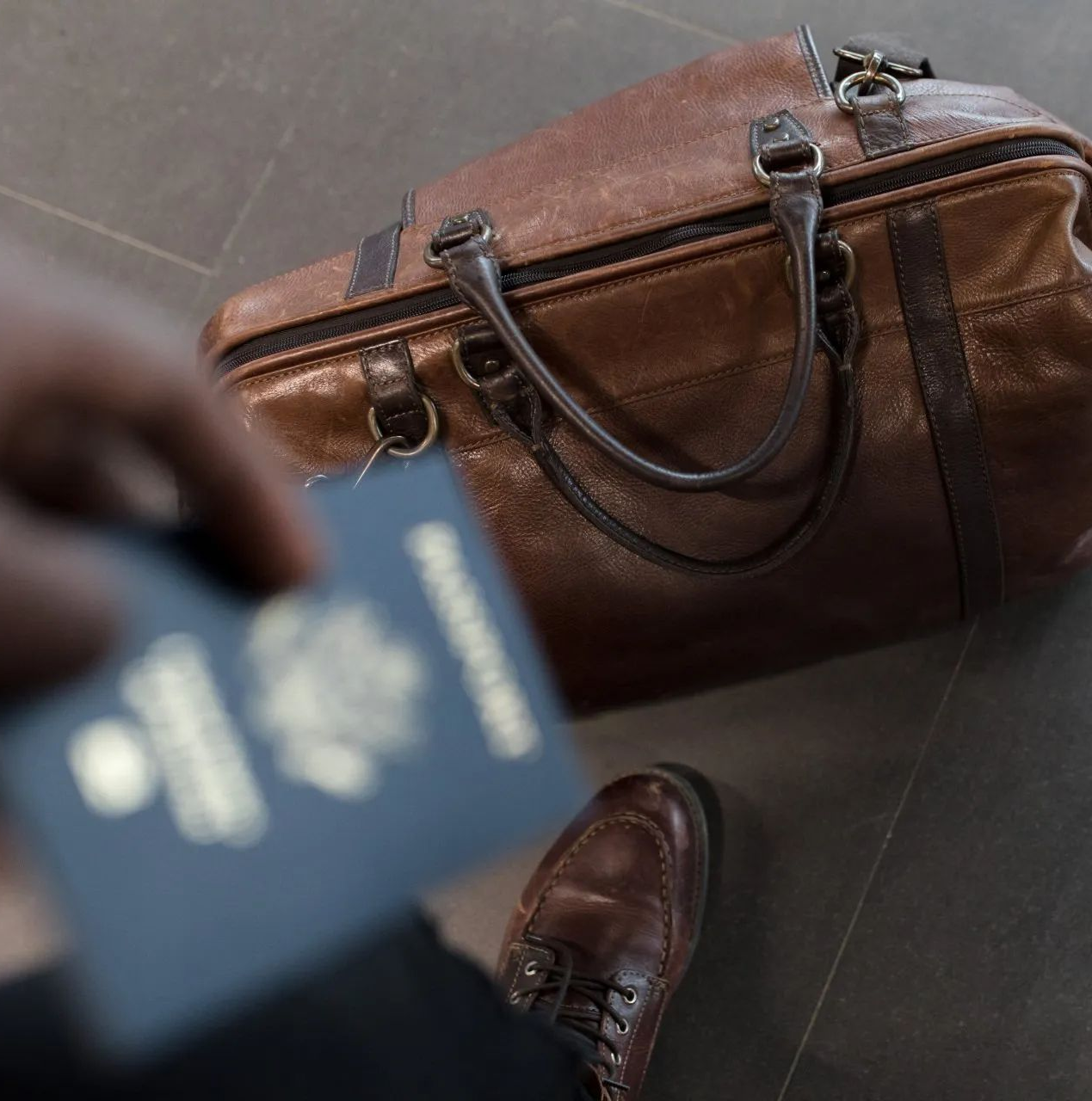 a person is holding a passport next to a brown duffel bag .