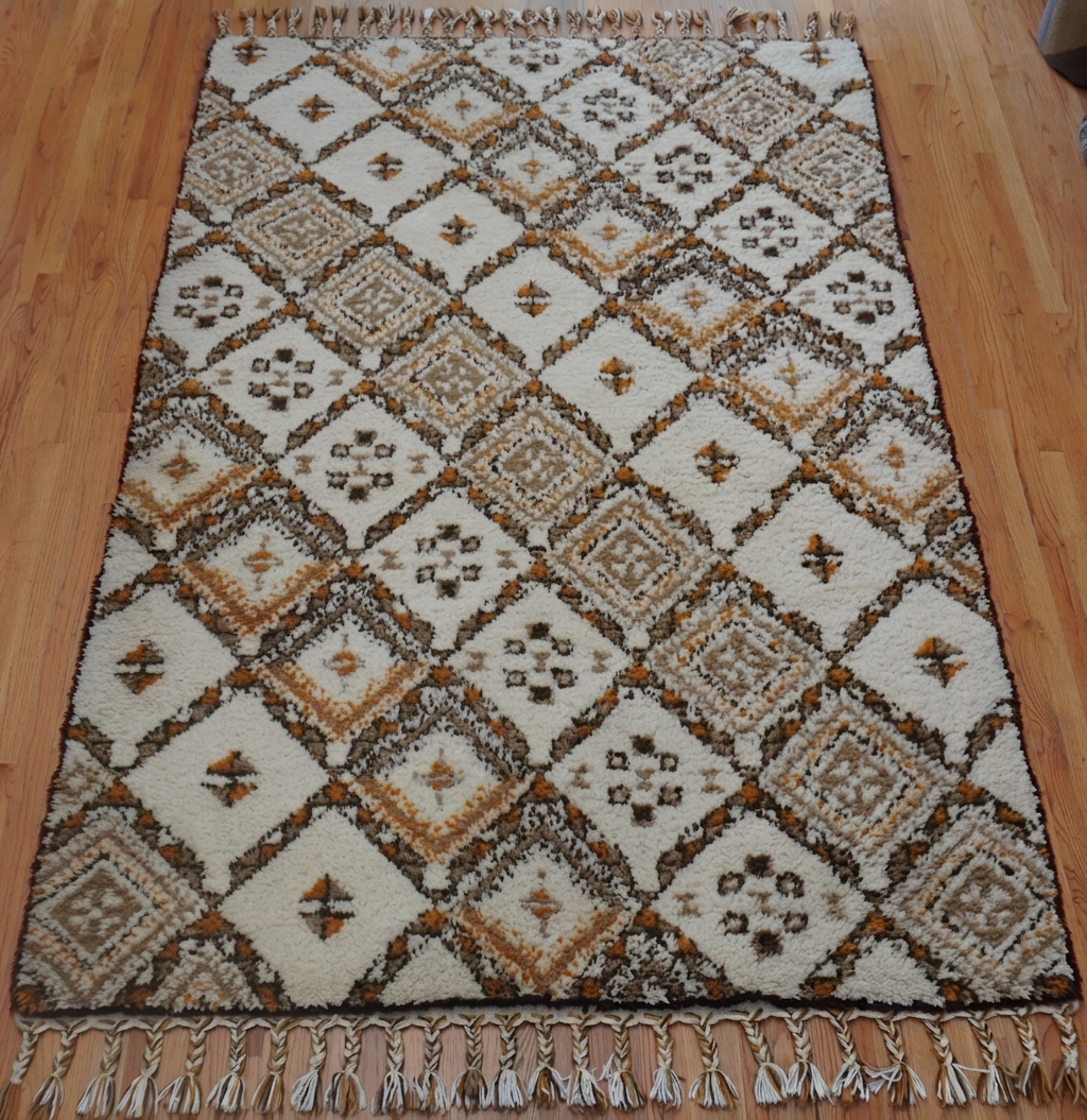 Patterned beige and brown hand-knotted rug with geometric diamonds on a wooden floor