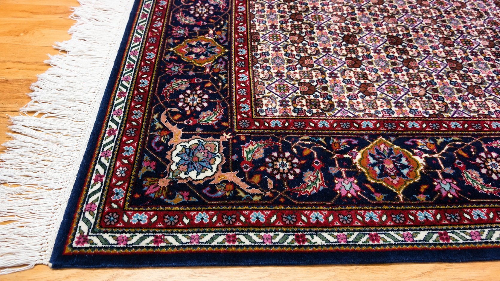 Patterned oriental rug with fringe on a light wooden floor, showing a dark border and floral design