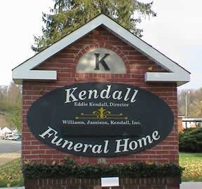 Sign for Kendall Funeral Home; brick with black oval, white text, and a “K” at the top.