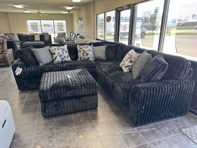 Black corduroy sectional sofa with matching ottoman in a furniture store.