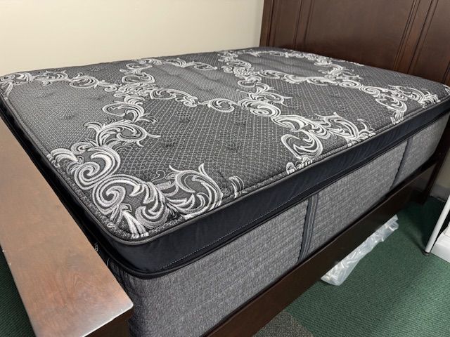 Dark gray mattress with white ornate design on a dark brown bed frame.