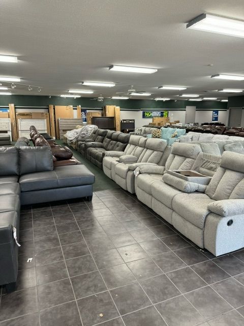 Furniture store interior with rows of couches and recliners, various colors and styles, on a tiled floor.