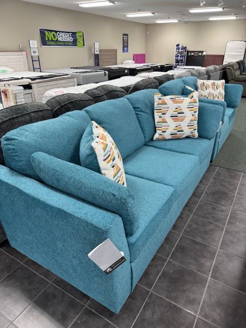Teal blue sofa with patterned throw pillows in a furniture store.