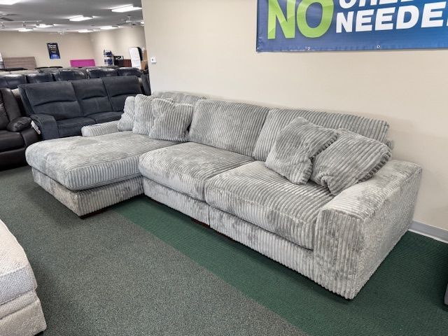 Gray corduroy sectional sofa with pillows in a furniture store.