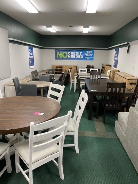 Furniture showroom with tables and chairs on a green carpet. Sign says