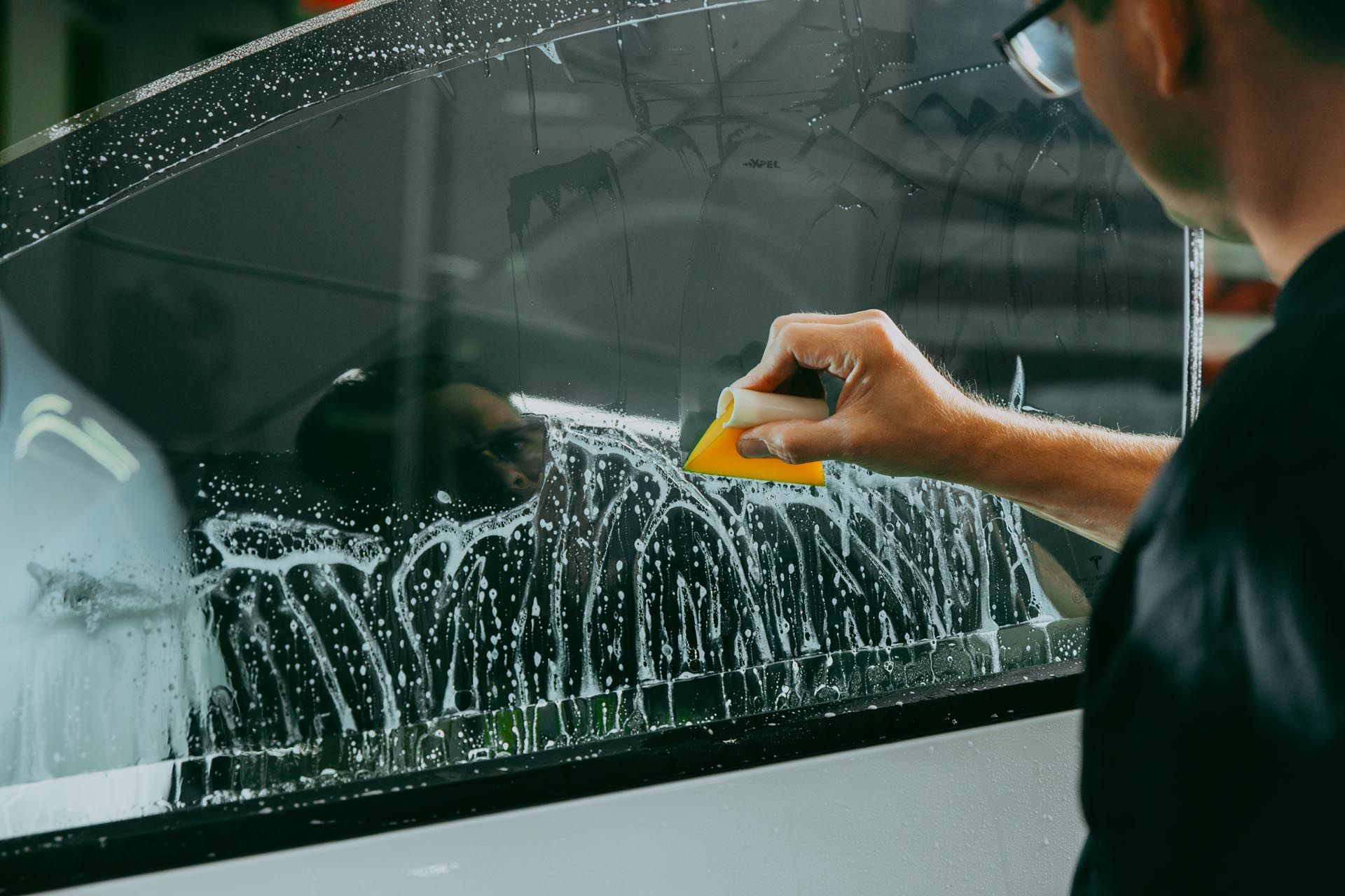 A man is cleaning a car window with a yellow sponge.