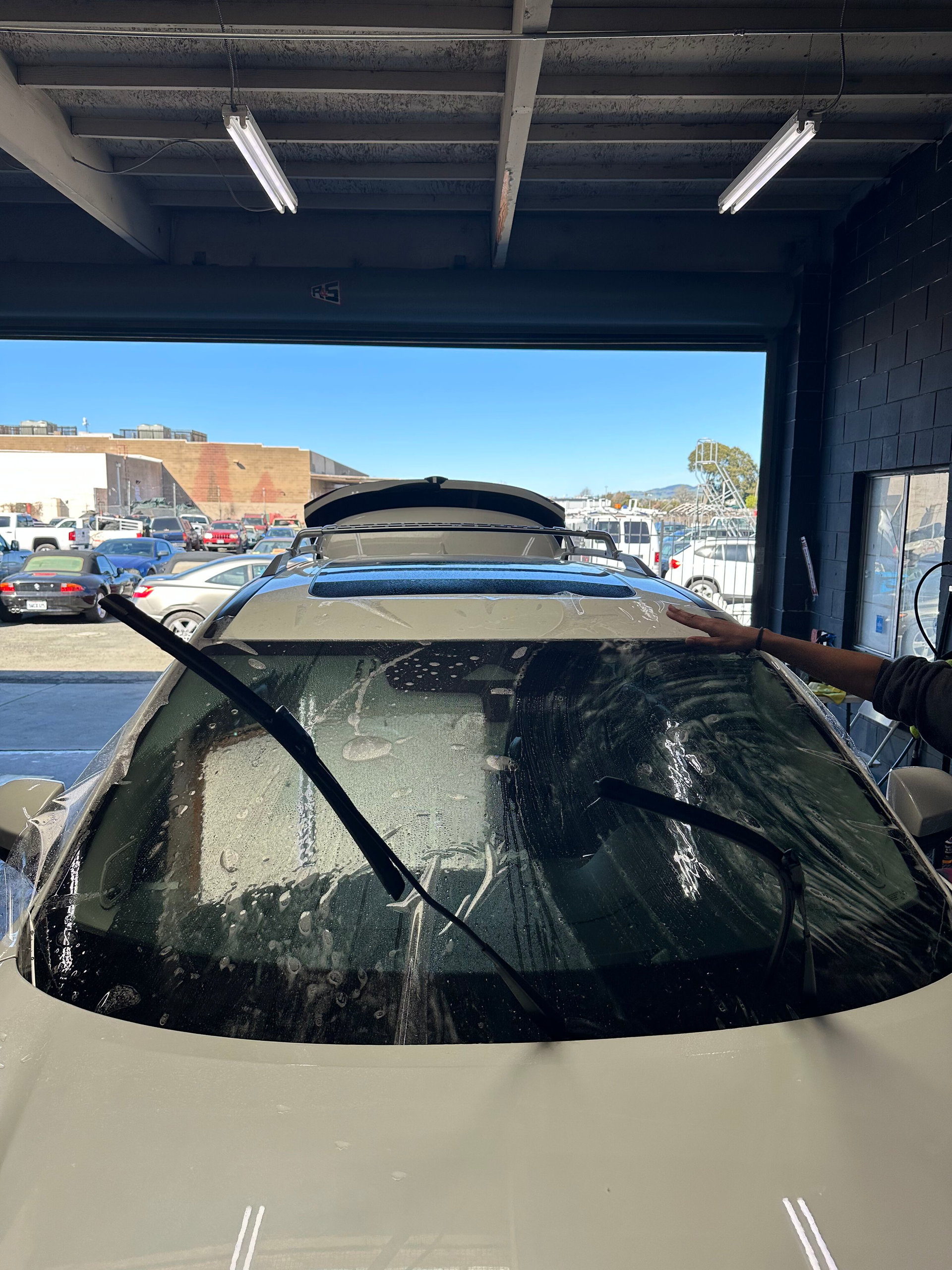 A person is cleaning the windshield of a car in a garage.