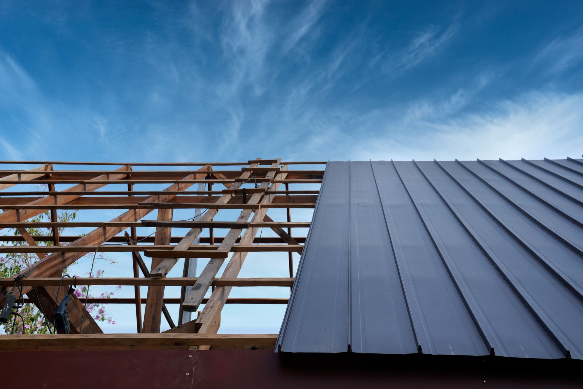 Roof construction: Metal panels being installed on wooden rafters against a blue sky.