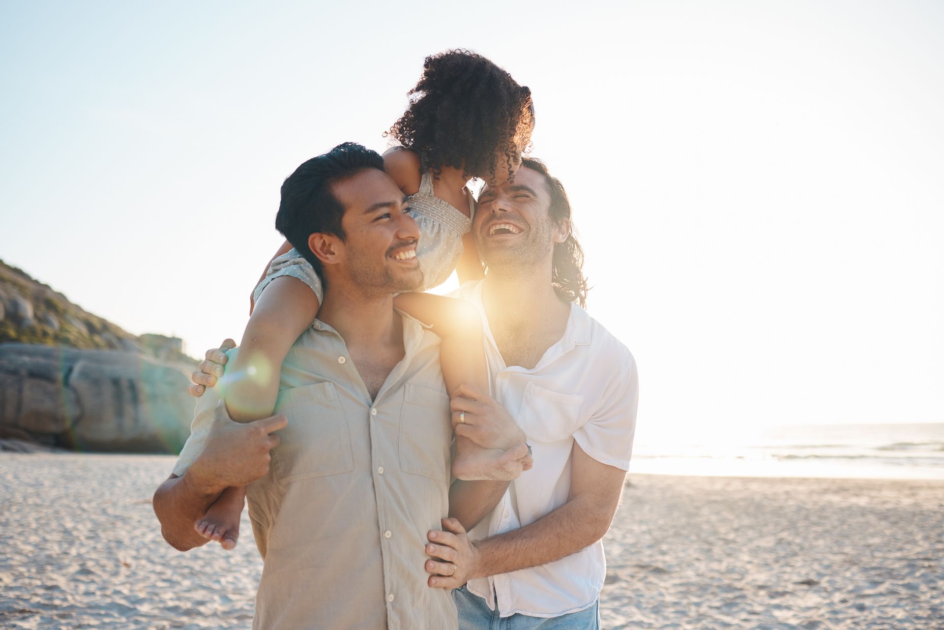 two dads and their child on a beach