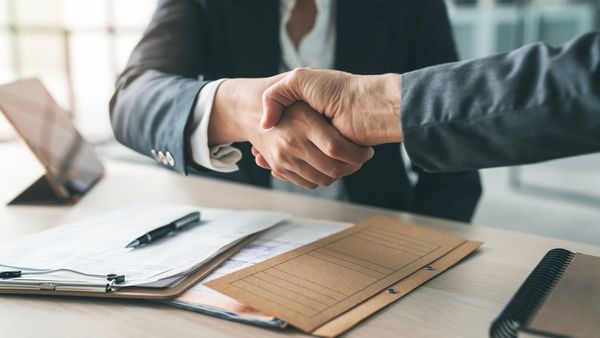 two people shaking hands over a stack of documents