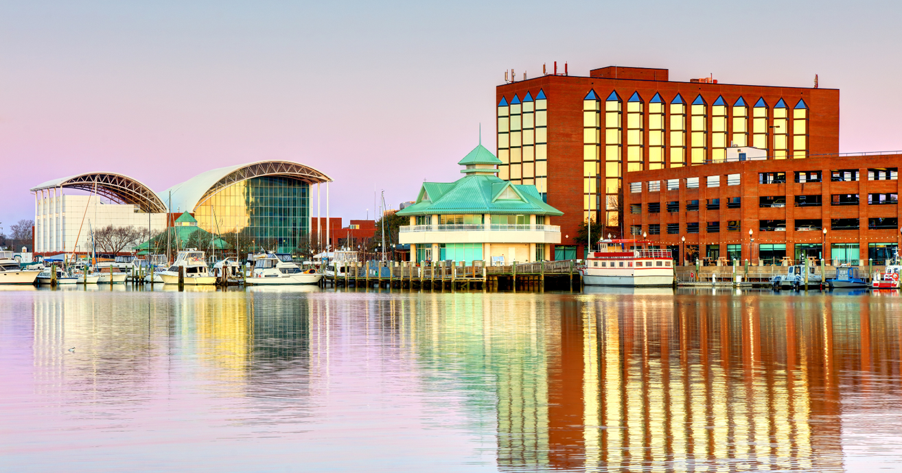 City skyline along a river at sunset; tall buildings, colorful sky reflecting on water. City skyline along a river at sunset; tall buildings, colorful sky reflecting on water.