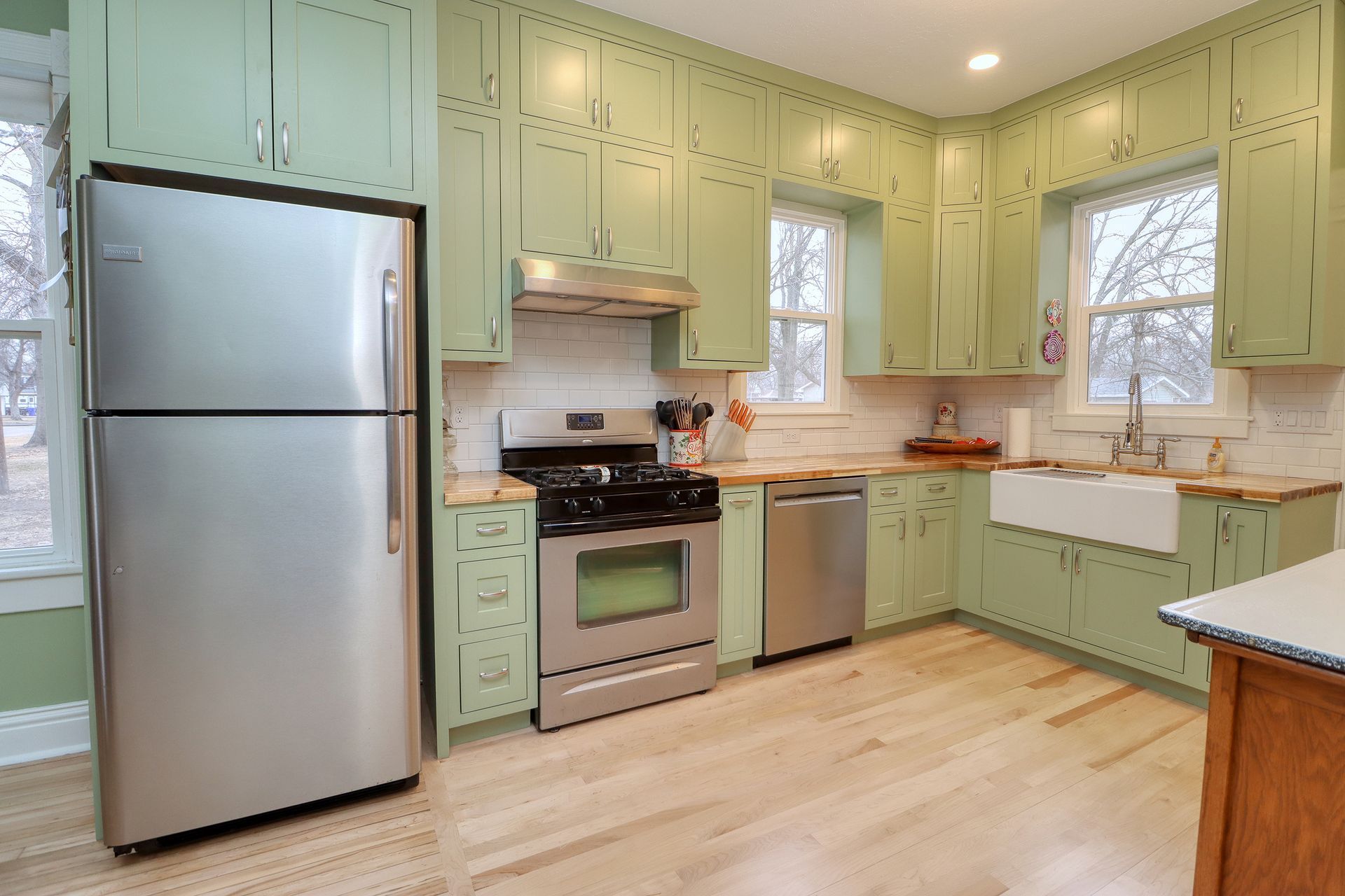 Bright kitchen with mint cabinets, stainless steel fridge, stove, dishwasher, and light wood floors.