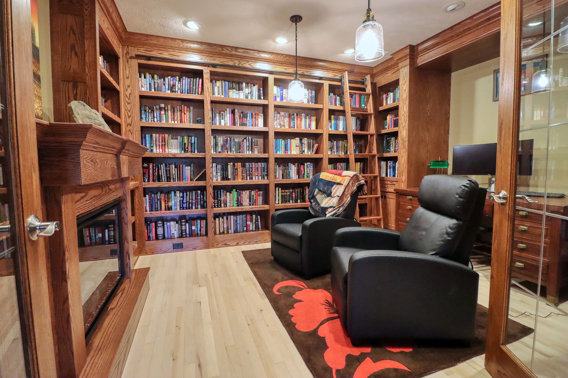 Cozy library with wall-to-wall bookshelves, two black chairs, and a fireplace on the left.