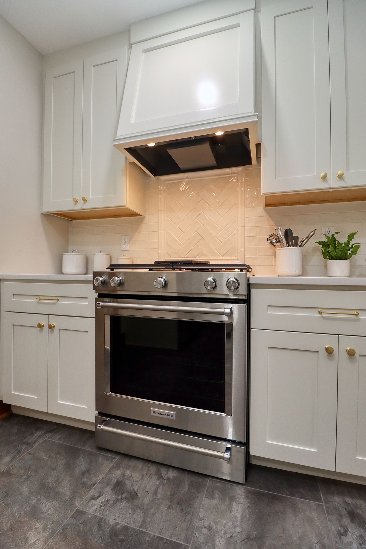 White kitchen with stainless steel stove and range hood, beige backsplash, and white cabinets