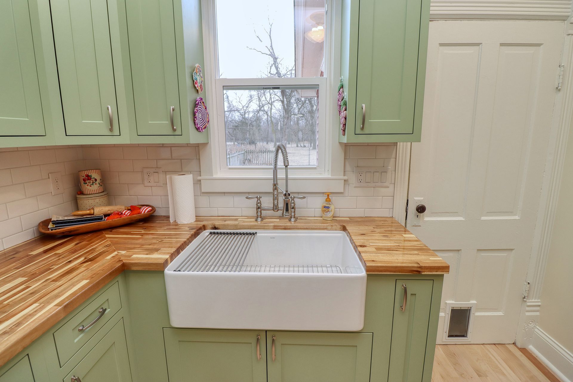 Bright kitchen with mint cabinets, wood countertops, farmhouse sink, and window above the sink.
