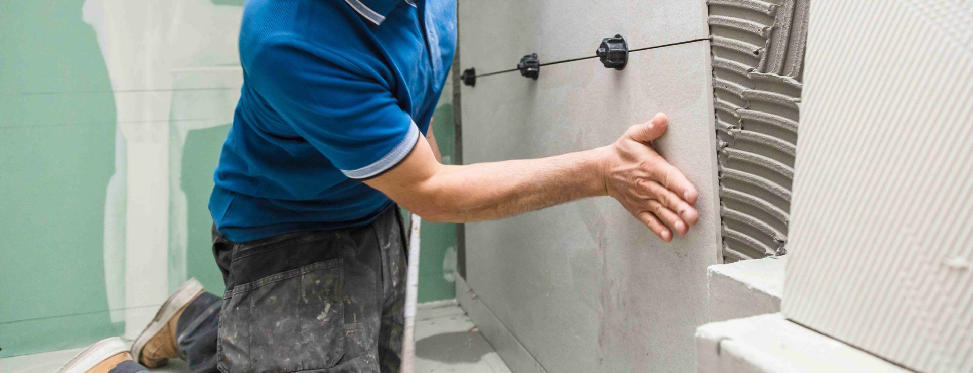 a worker installing large gray wall tiles in a bathroom or kitchen setting.