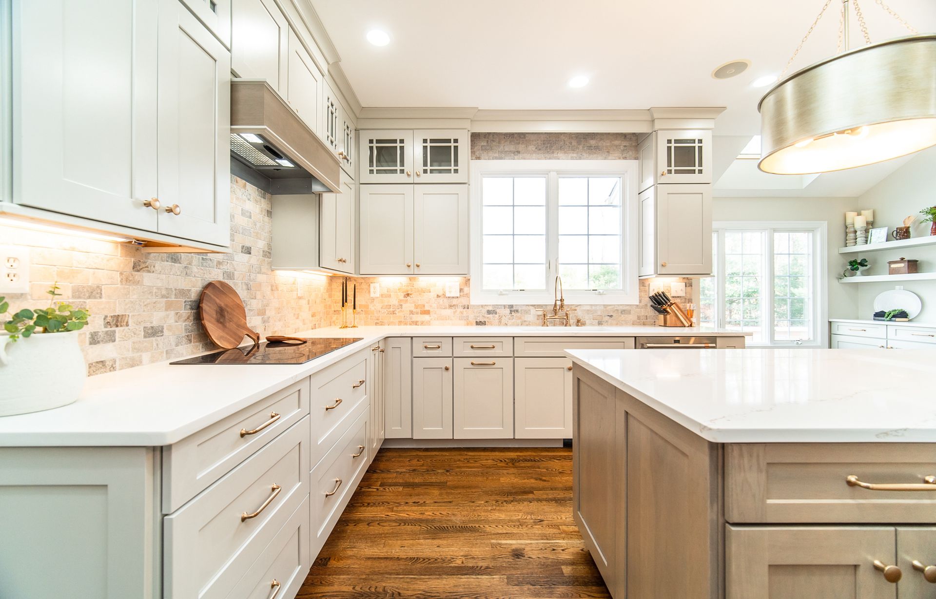 Bright modern kitchen with white cabinets, marble countertops, wood floor, and large window over sink