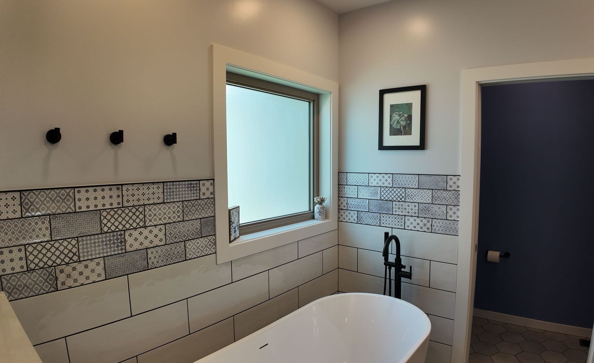 Modern bathroom with a freestanding tub, mosaic tile accents, window, and dark open door