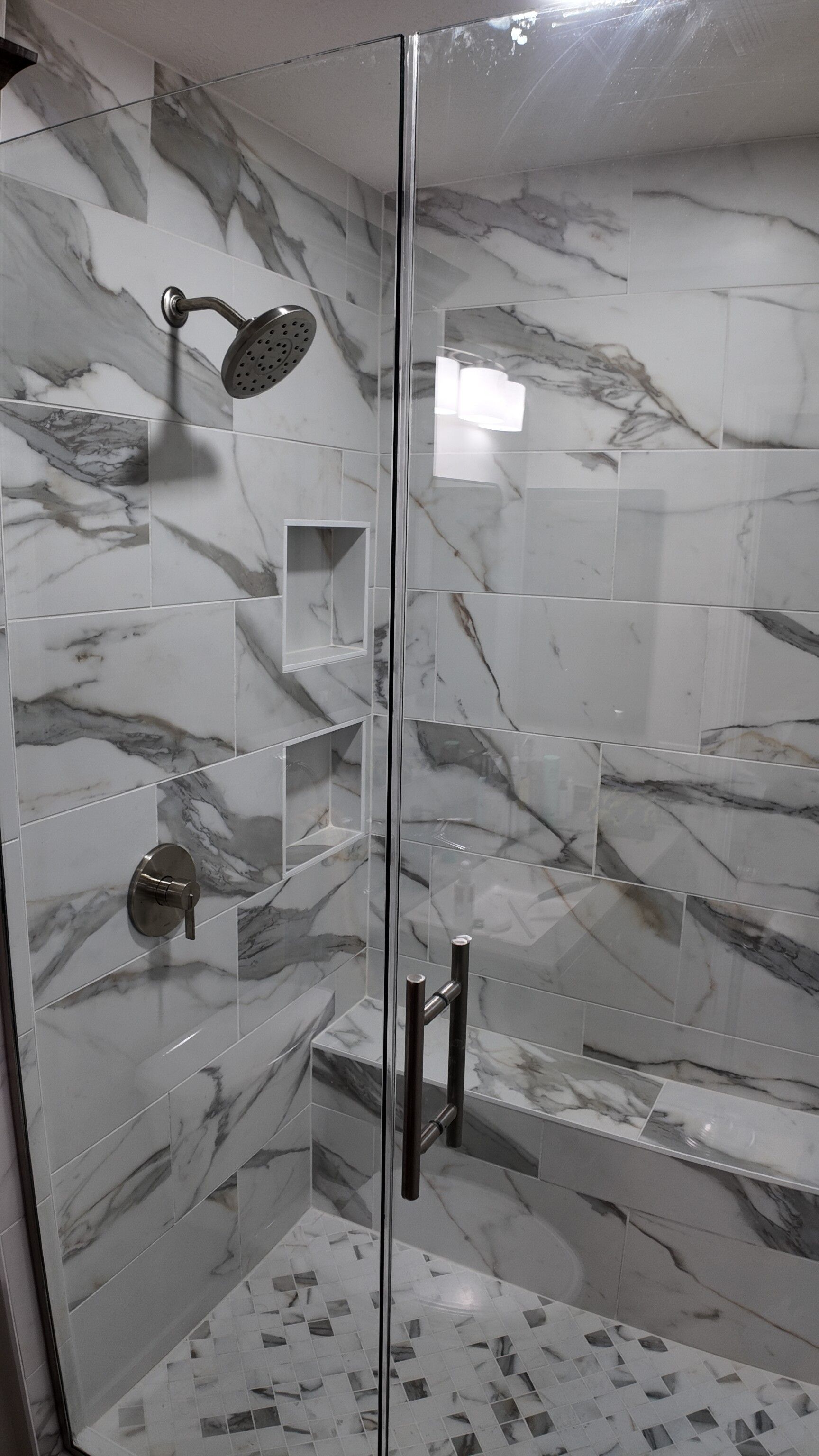 Modern tiled walk-in shower with glass doors, marble-look walls, and chrome fixtures